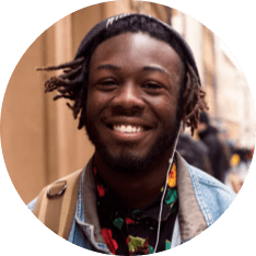 Smiling young man with dreadlocks wearing a beanie and headphones on a city street